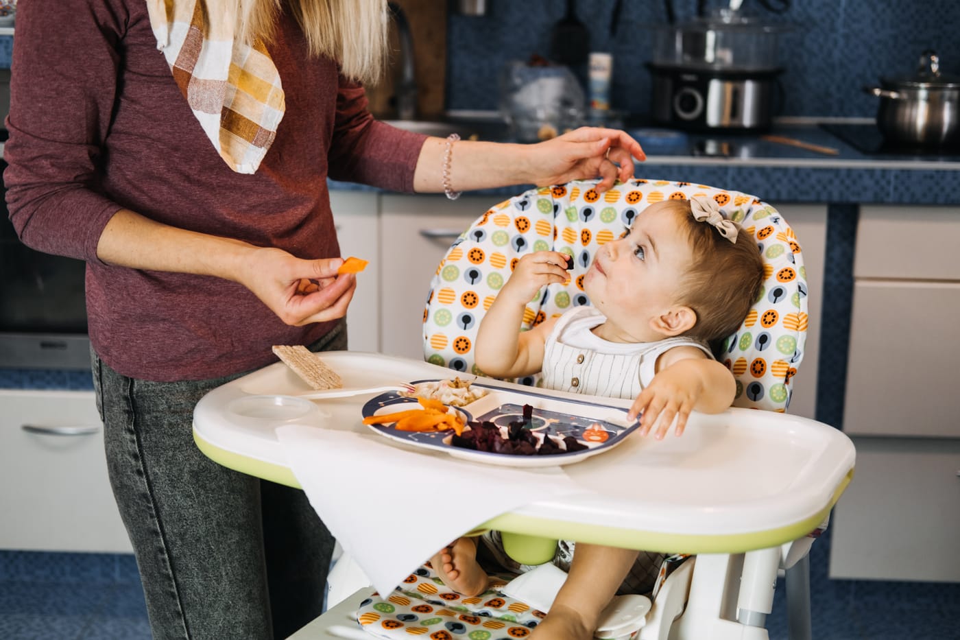 bebé comiendo trozos de comida bajo supervisión de un adulto