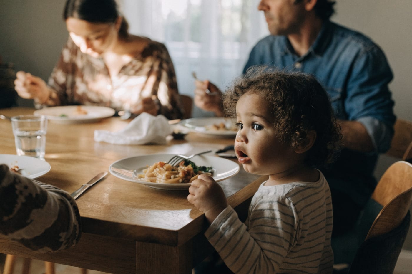 niño pequeño sentado a la mesa familiar explorando su plato de comida