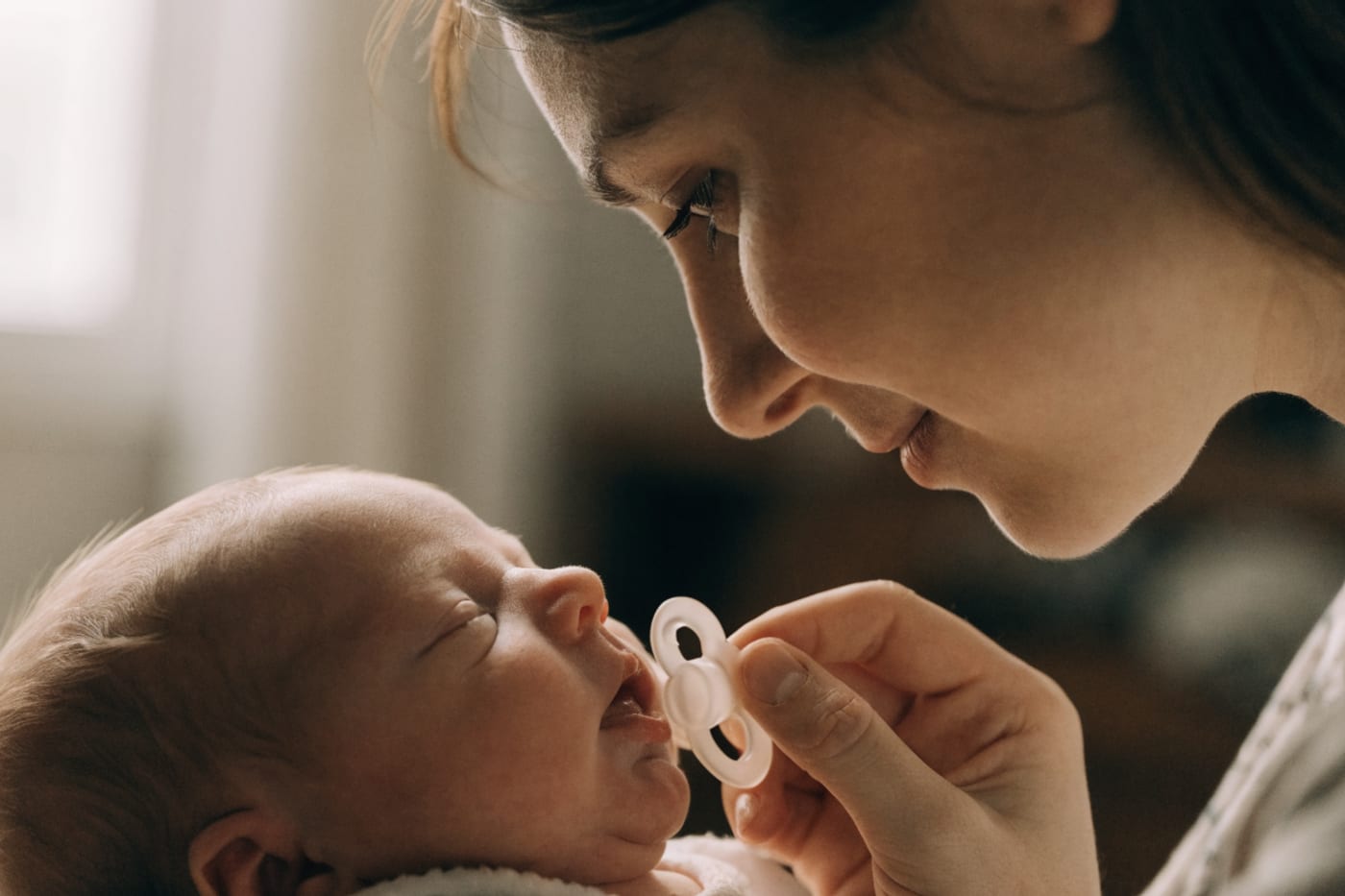 madre observando a su bebé mientras se prende al pecho con un chupete cerca