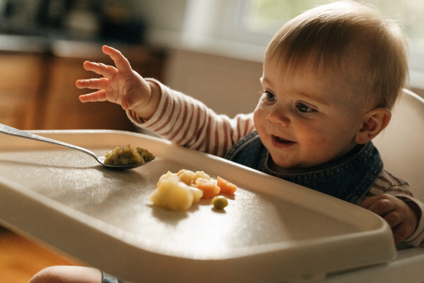 bebé sentado a la mesa comiendo con cuchara y con trozos de alimento en su plato