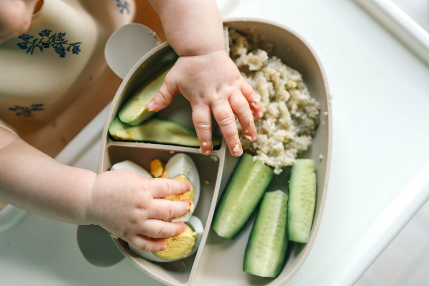 Bebé sosteniendo comida cortada al estilo Baby Led Weaning en su silla alta